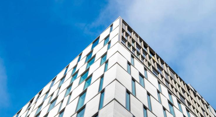 The corner of a tall glass and metal building against a blue sky
