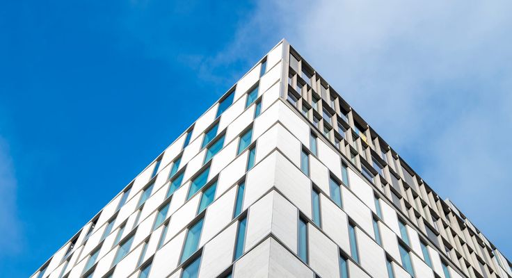 The corner of a tall glass and metal building against a blue sky