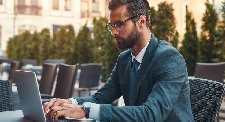 A man in a suit working on a laptop at an outdoor table