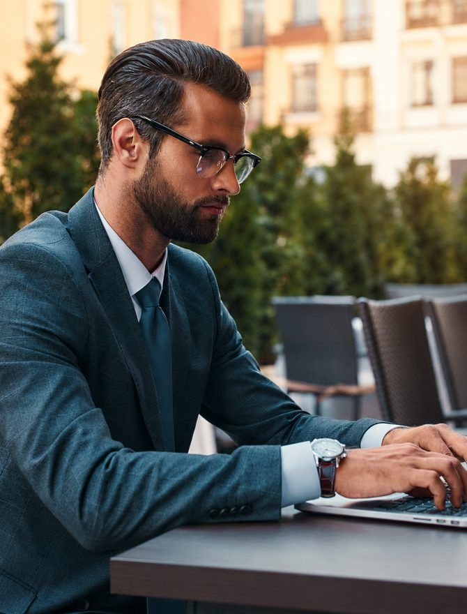 A man in a suit working on a laptop at an outdoor table