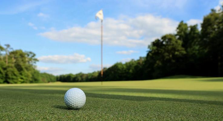 A golf ball on the green beside the hole and flag