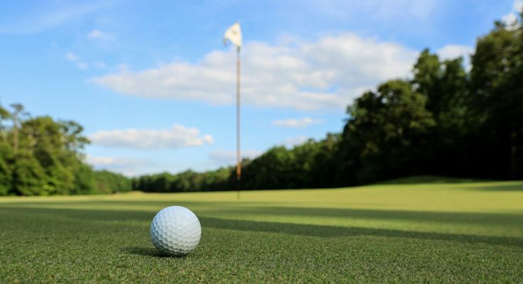 A golf ball on the green beside the hole and flag
