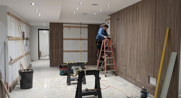 A joiner on a stepladder fitting timber wall panelling in a room under construction
