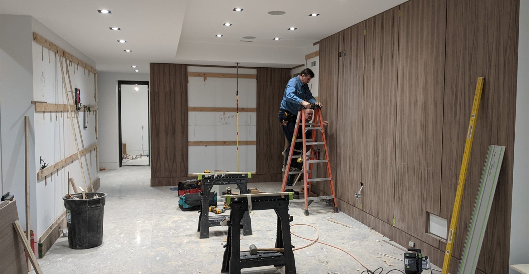 A joiner on a stepladder fitting timber wall panelling in a room under construction