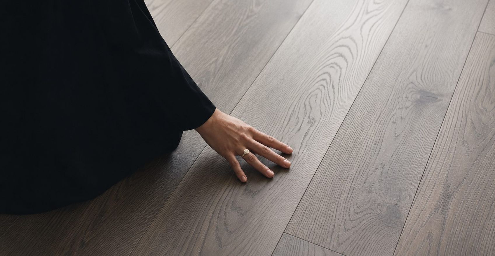 A hand resting on newly laid wide-plank wood flooring