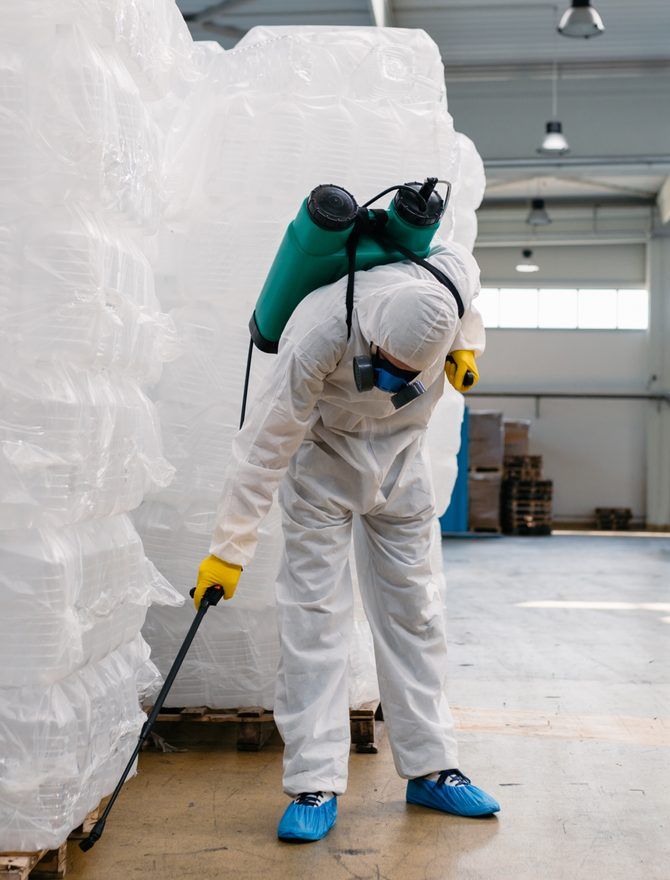 A technician in a protective suit treating the floor of a warehouse