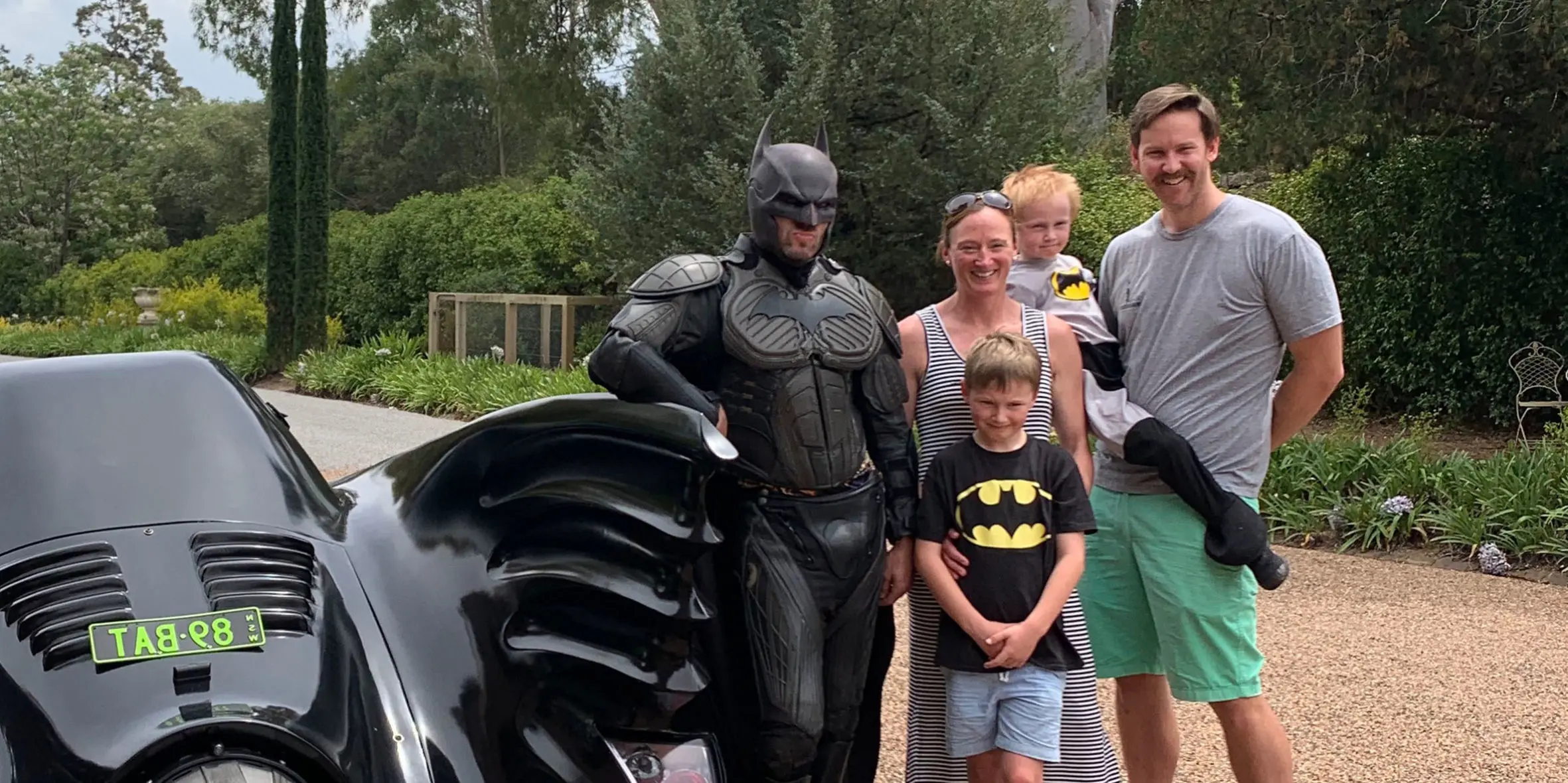 Make-A-Wish kid Rory stands with his family and batman, next to the batmobile