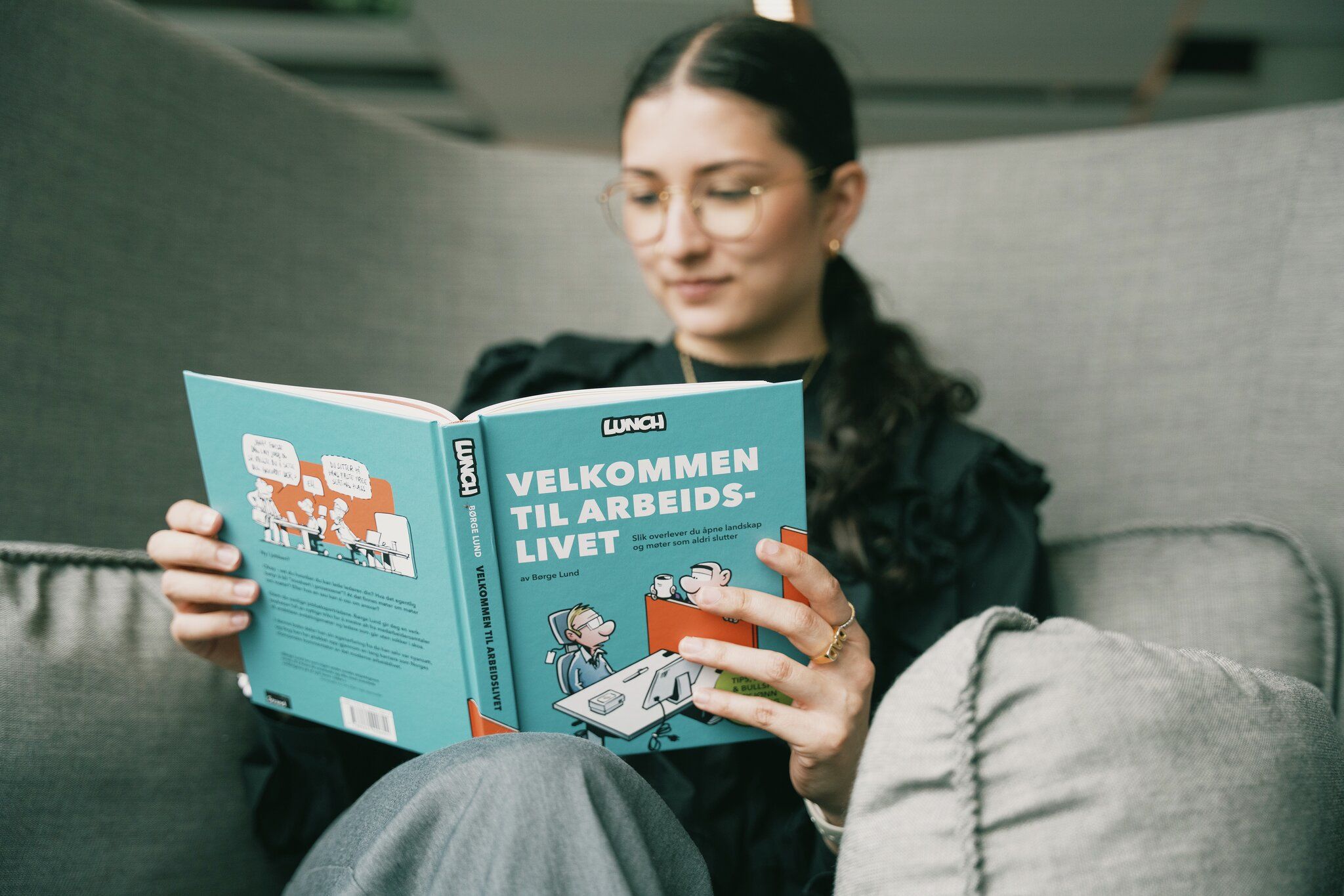 Ung kvinne leser tegneserie med tittel «Velkommen til arbeidslivet»