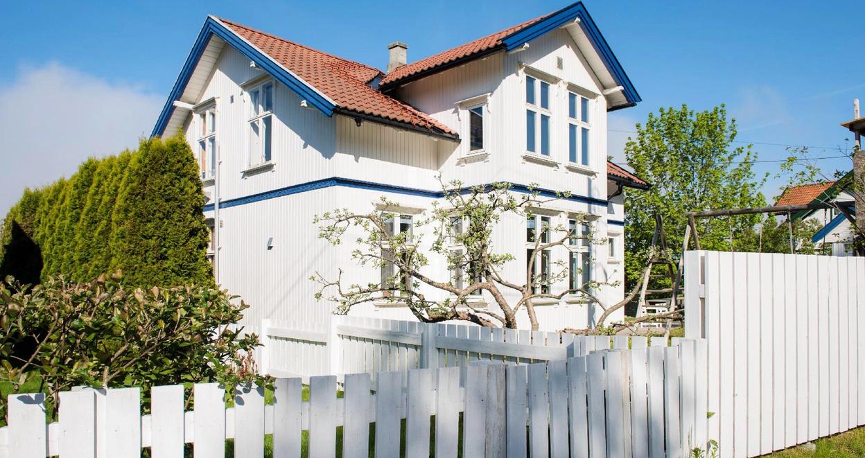 En godt vedlikeholdt hvit villa med frodig grønn hage