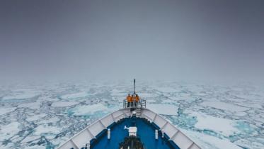 Et mannskap står ved baugen på en båt som kjører gjennom drivis