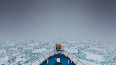 Et mannskap står ved baugen på en båt som kjører gjennom drivis