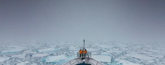 Et mannskap står ved baugen på en båt som kjører gjennom drivis