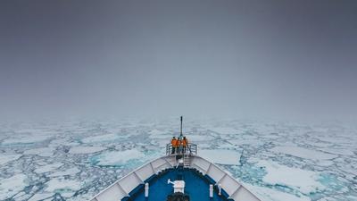 Et mannskap står ved baugen på en båt som kjører gjennom drivis