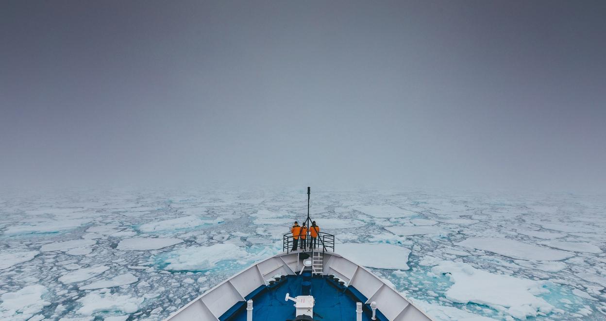 Et mannskap står ved baugen på en båt som kjører gjennom drivis