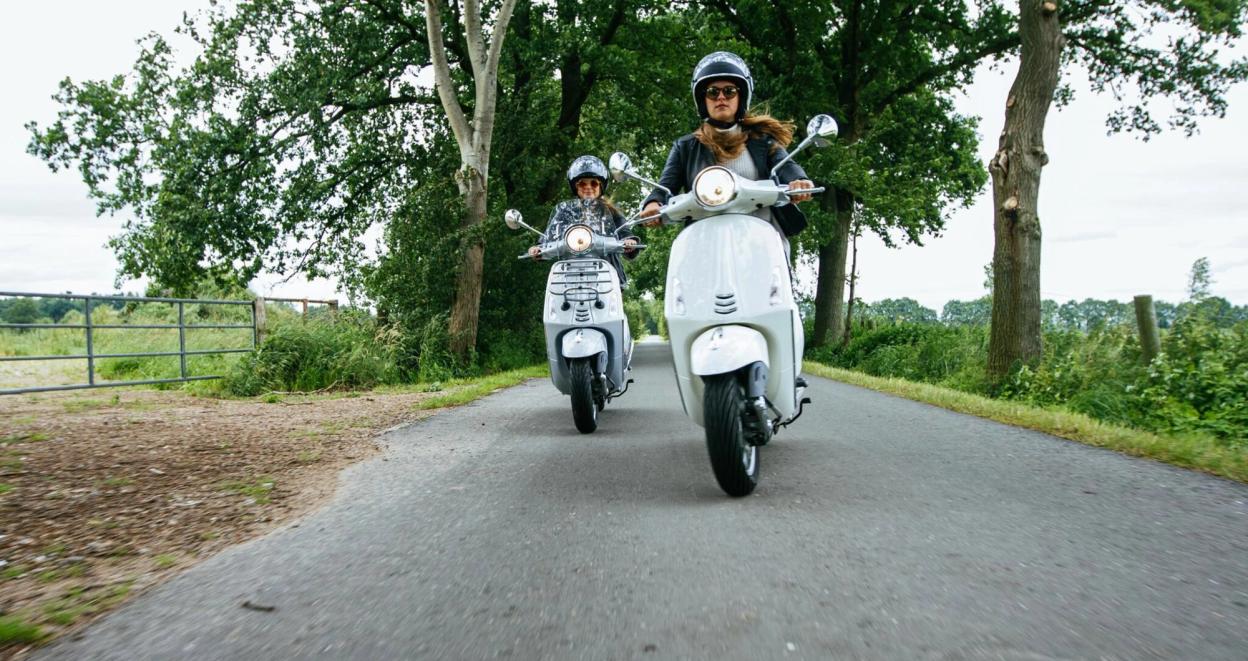 To personer kjører scootere langs en landevei