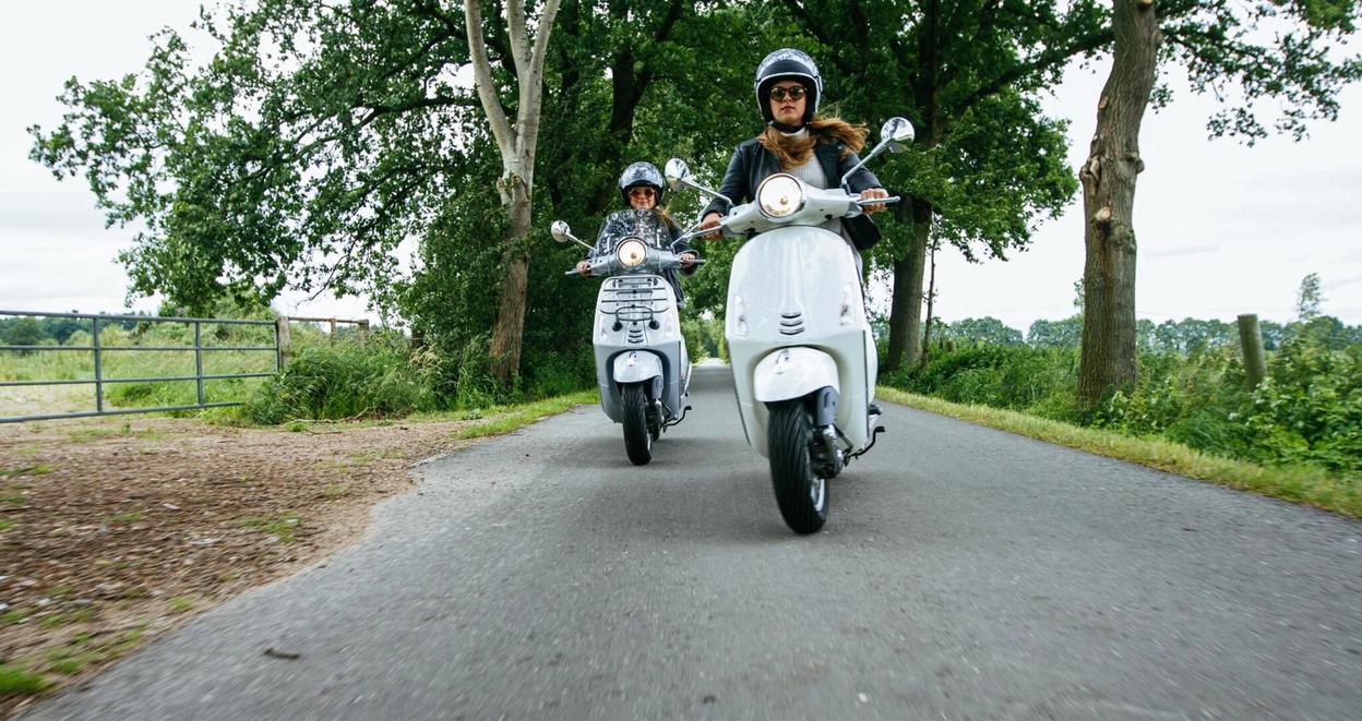 To personer kjører scootere langs en landevei