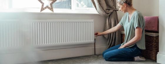 Kvinne stiller termostaten på radiatoren i huset