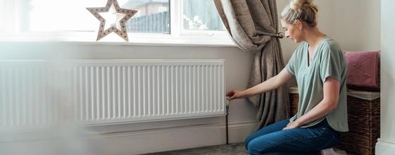Kvinne stiller termostaten på radiatoren i huset