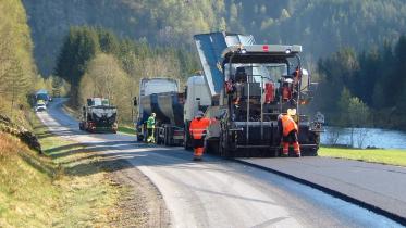 Anleggsarbeidere legger ny asfalt langs en landevei
