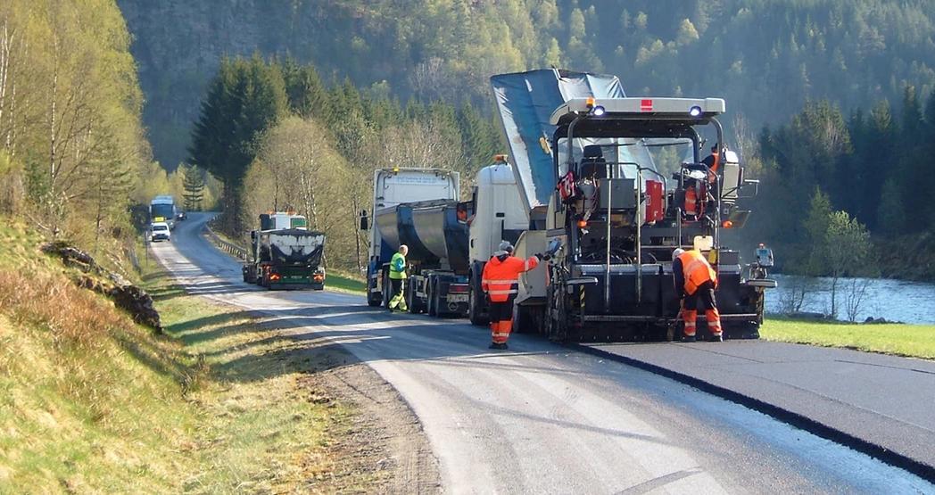 Anleggsarbeidere legger ny asfalt langs en landevei