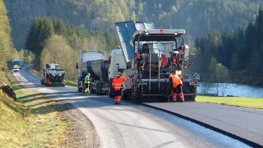 Anleggsarbeidere legger ny asfalt langs en landevei