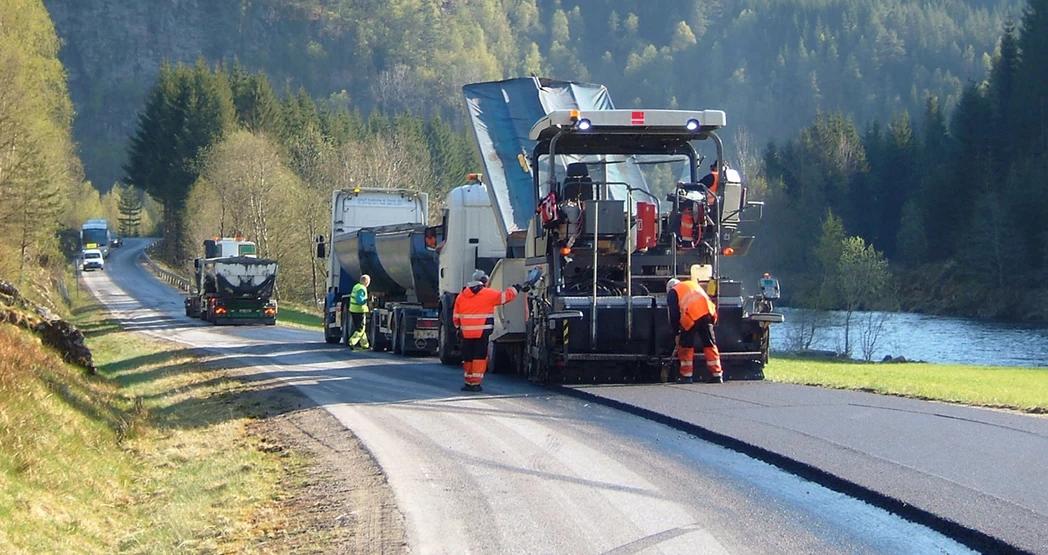 Anleggsarbeidere legger ny asfalt langs en landevei