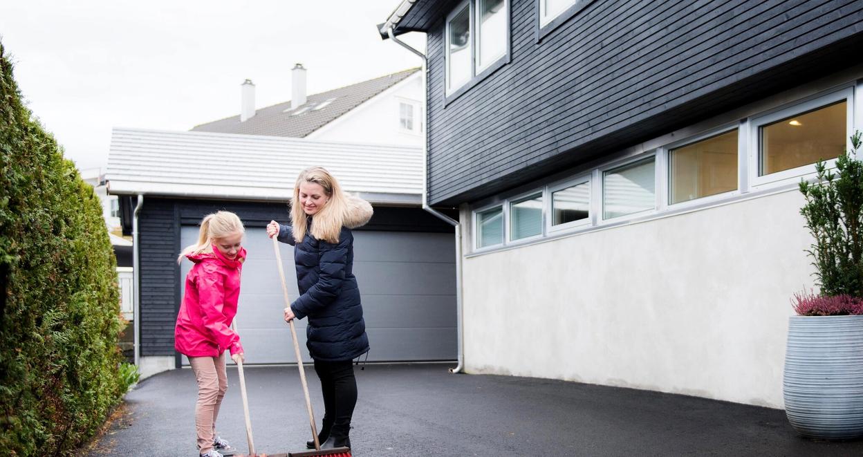 Mor og datter feier grus og løv fra parkeringsplassen ved huset.