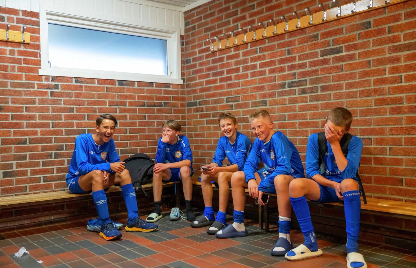 Gutter som spiller fotball sitter i garderoben.