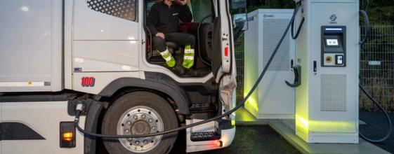 Sjåfør som drikker kaffe mens lastebil lader elektrisk lastebil