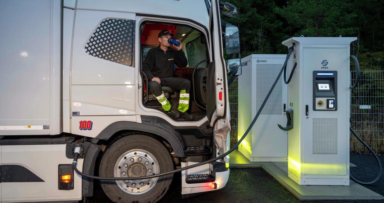 Sjåfør som drikker kaffe mens lastebil lader elektrisk lastebil