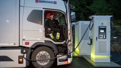 Sjåfør som drikker kaffe mens lastebil lader elektrisk lastebil