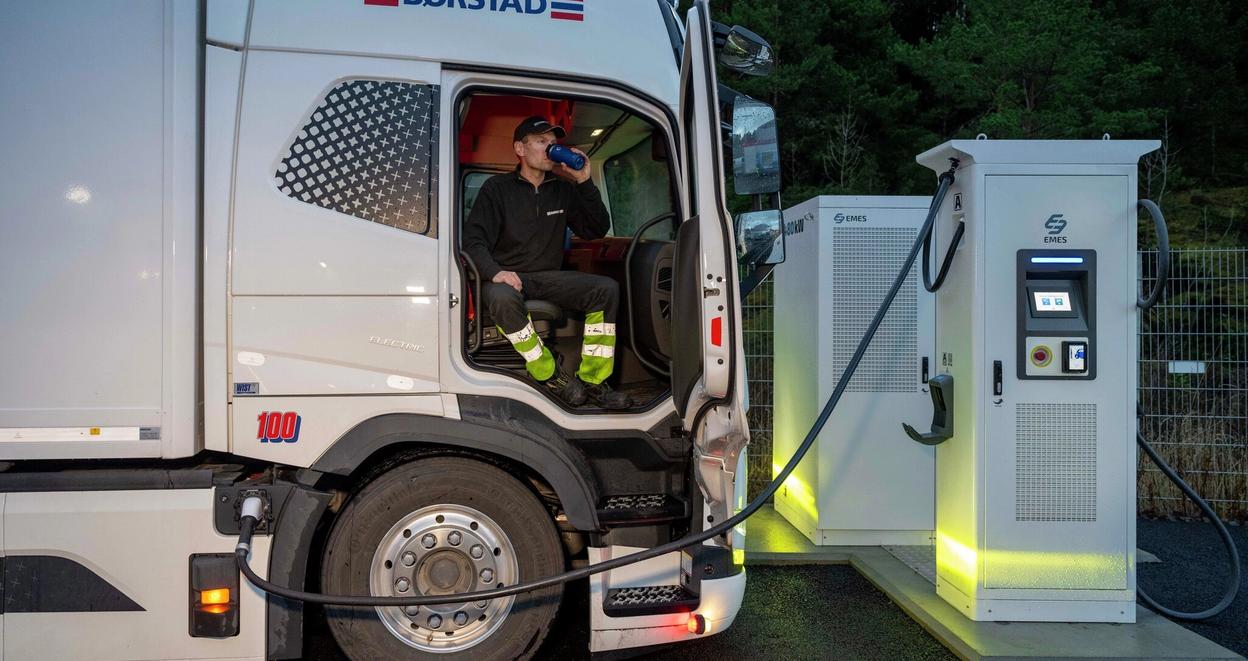Sjåfør som drikker kaffe mens lastebil lader elektrisk lastebil