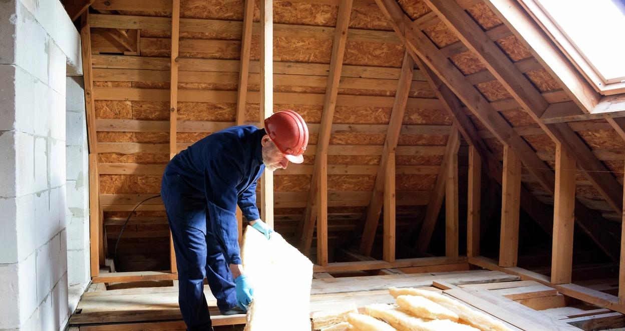 Mann legger ekstra isolasjon på loft i eldre bolig
