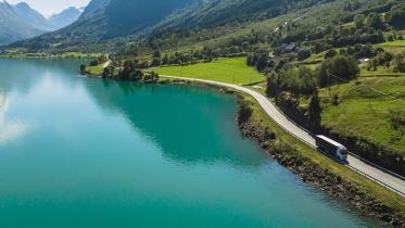 Lastebil kjører langs en distriktsvei i et frodig fjell- og fjordlandskap