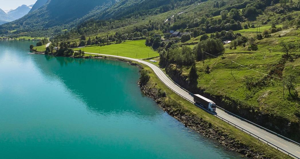 Lastebil kjører langs en distriktsvei i et frodig fjell- og fjordlandskap