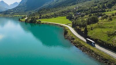 Lastebil kjører langs en distriktsvei i et frodig fjell- og fjordlandskap