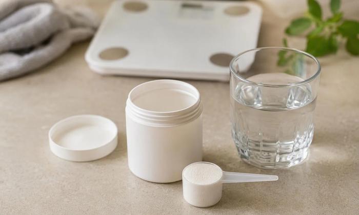 A plain supplement container and scoop beside water.