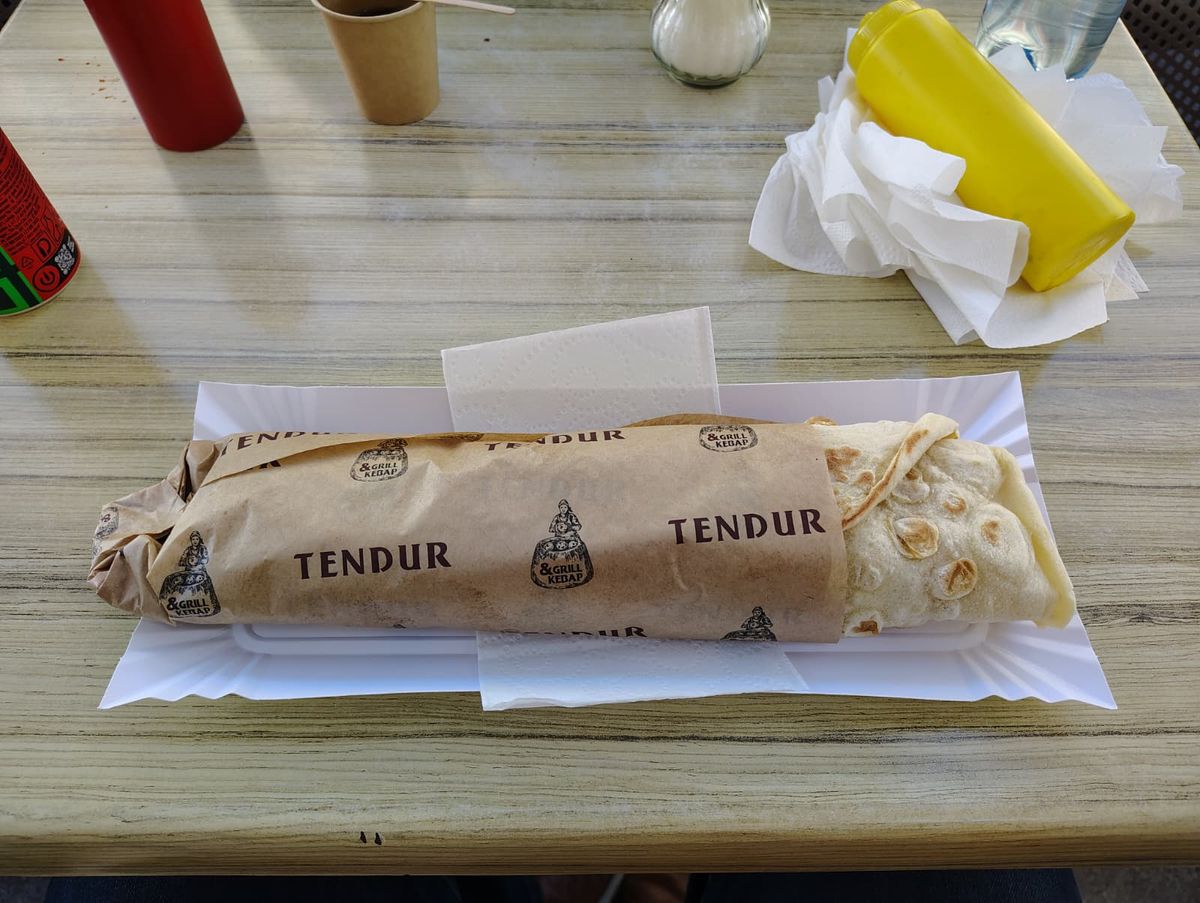 Lavash-wrapped kebab sitting on a table wrapped in paper that says Tendur