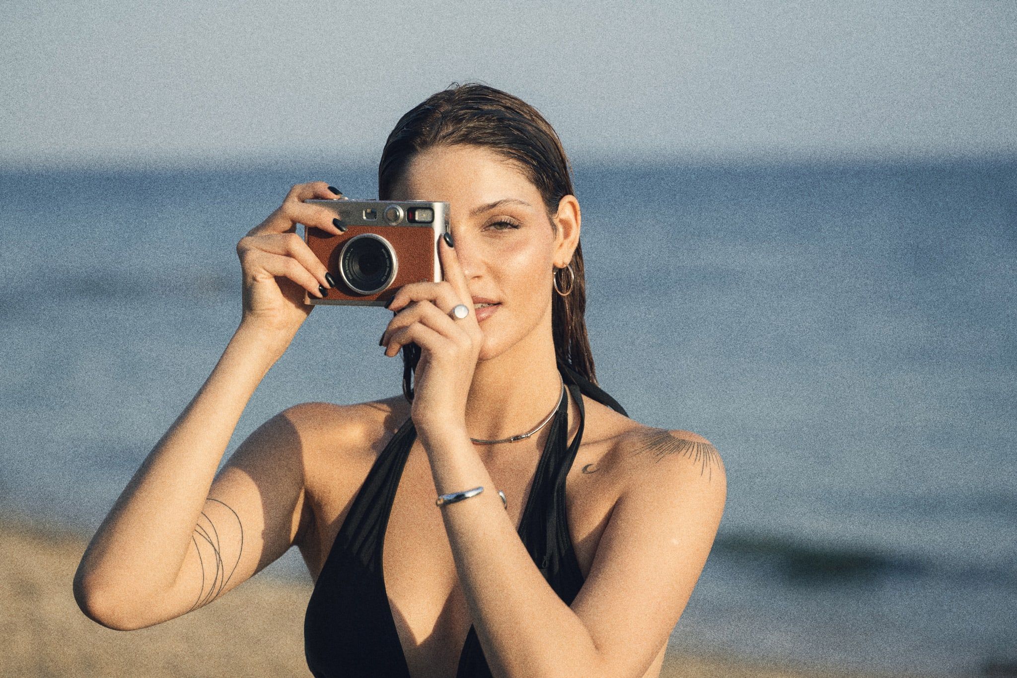 Woman on a beach holding a compact film camera to her eye
