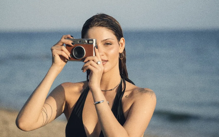 Woman on a beach holding a compact film camera to her eye