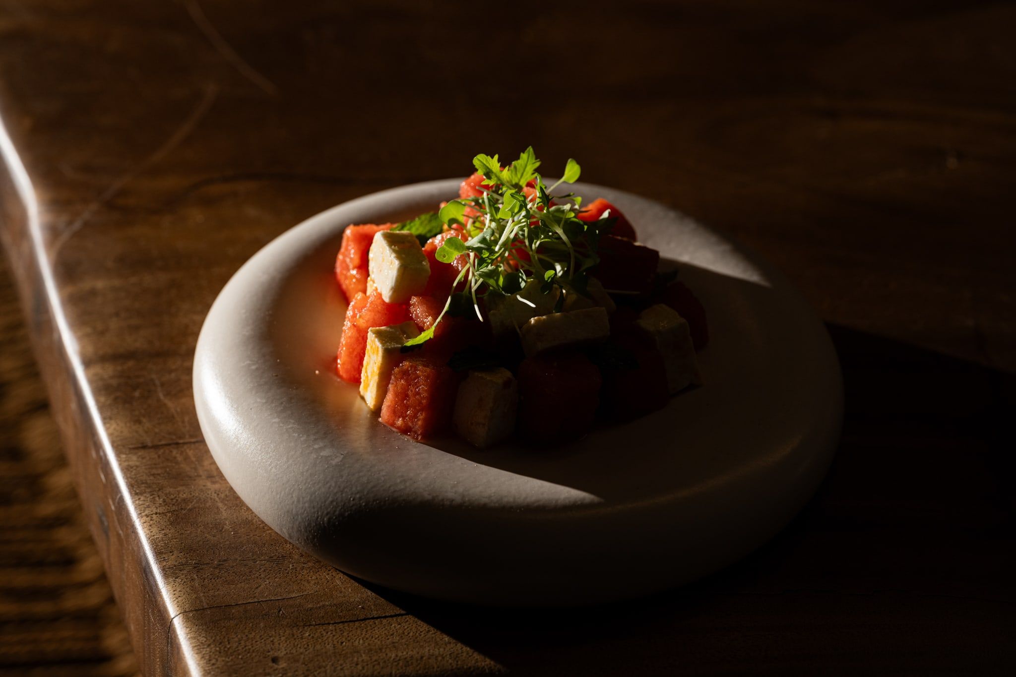 Plated watermelon and feta dish on a stone bowl, dark wooden table