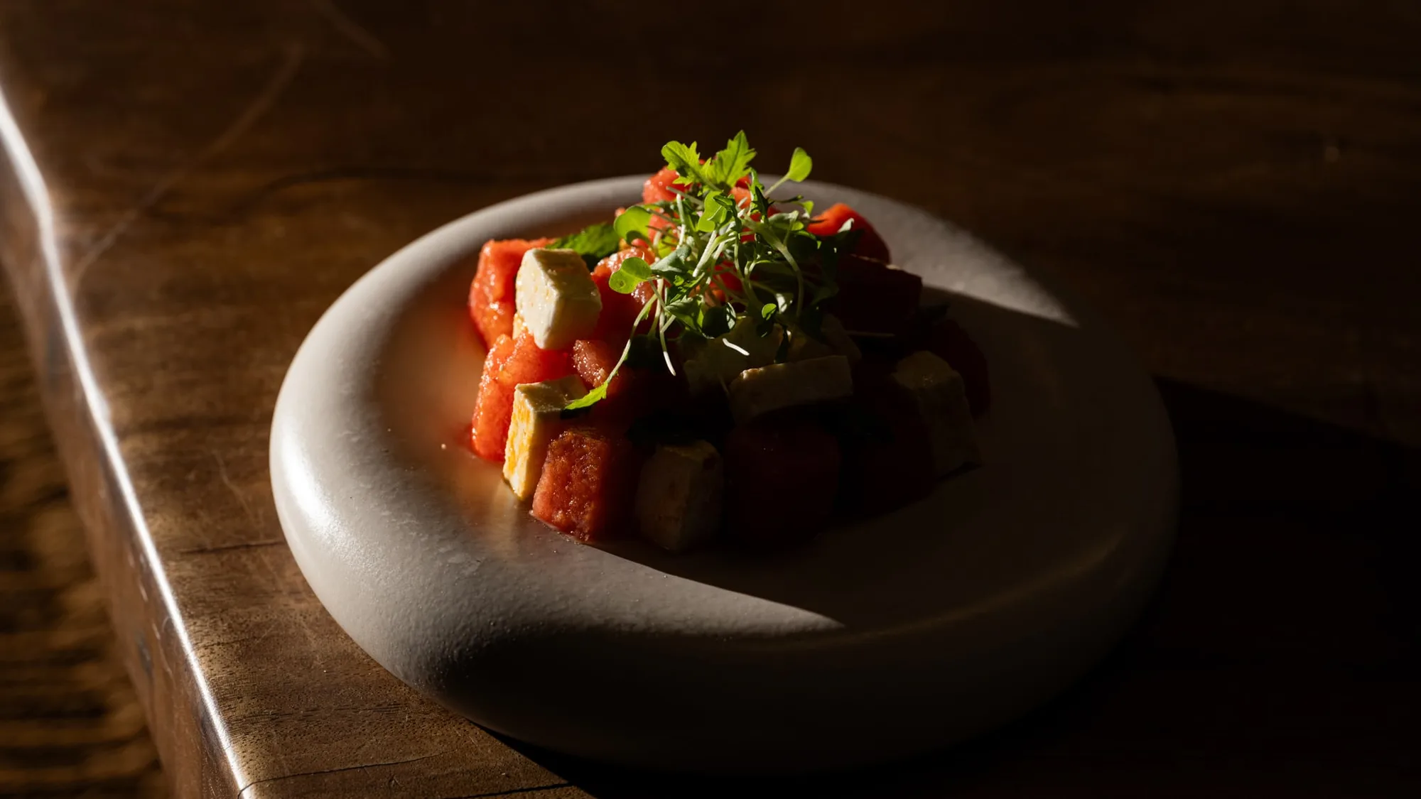 Plated watermelon and feta dish on a stone bowl, dark wooden table