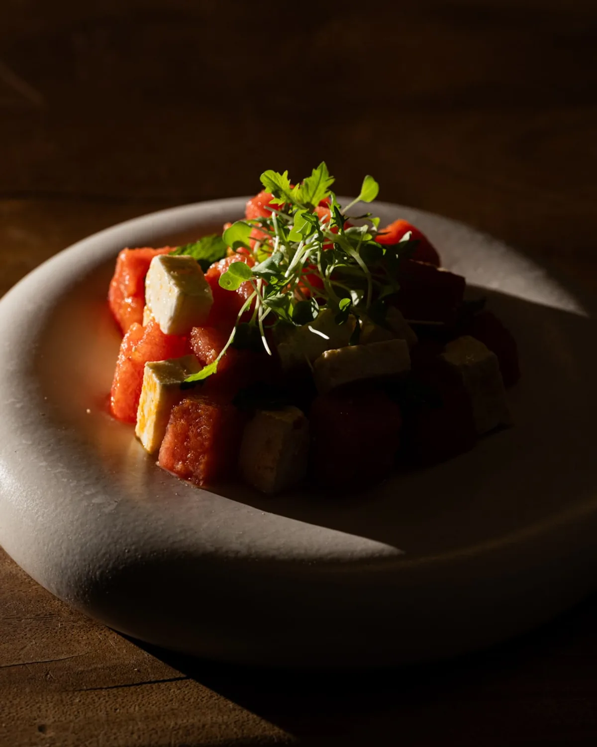 Plated watermelon and feta dish on a stone bowl, dark wooden table