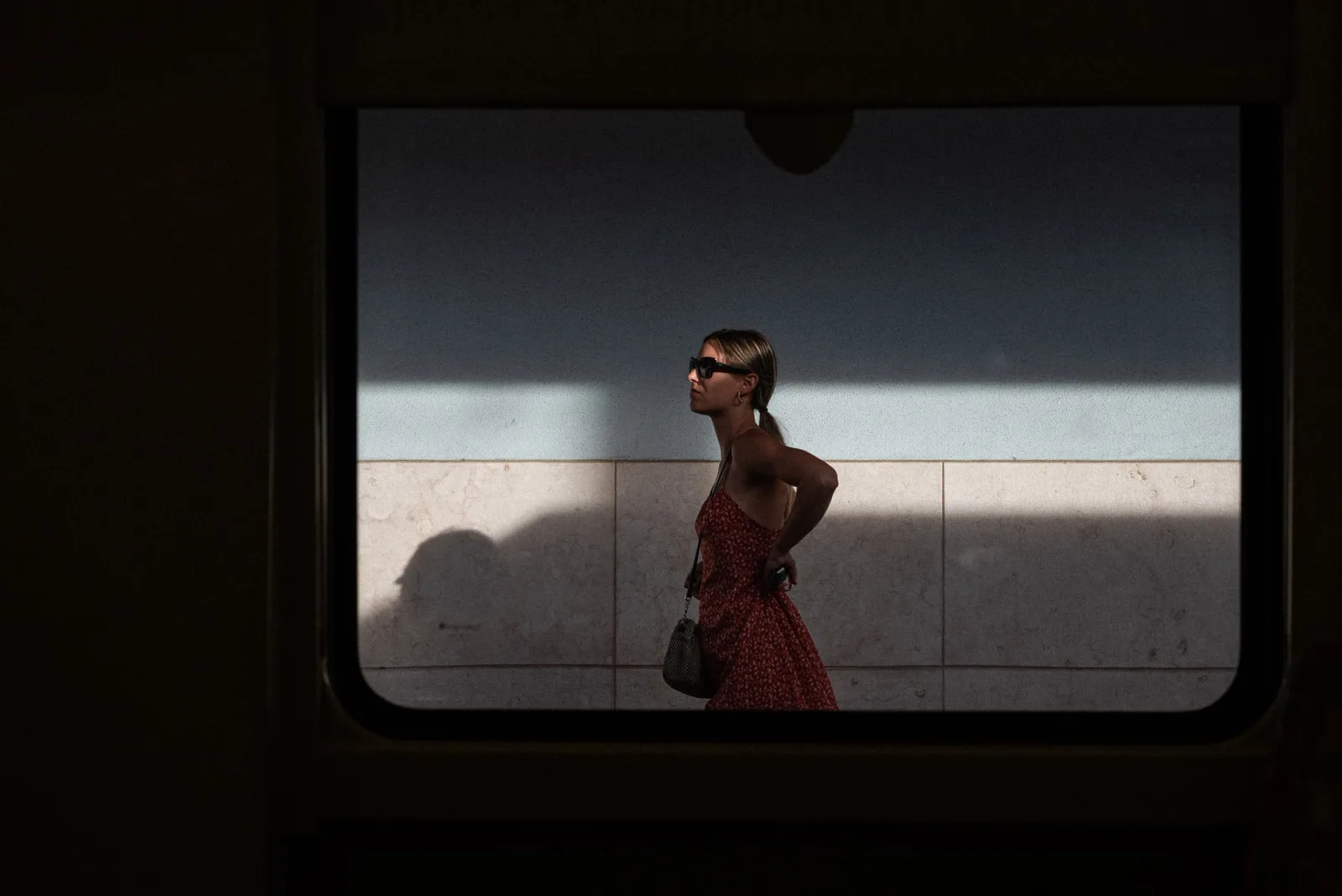 Woman in a red dress walking past, seen through a dark rounded window frame