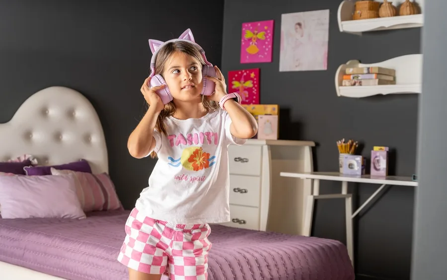 Child in printed pyjamas standing on a bed wearing cat-ear headphones