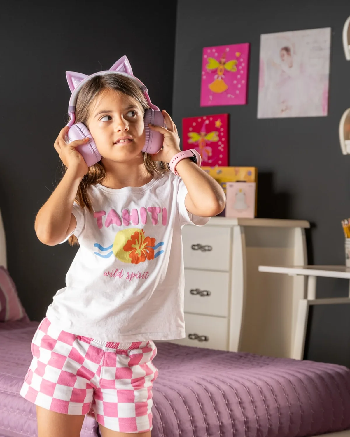 Child in printed pyjamas standing on a bed wearing cat-ear headphones