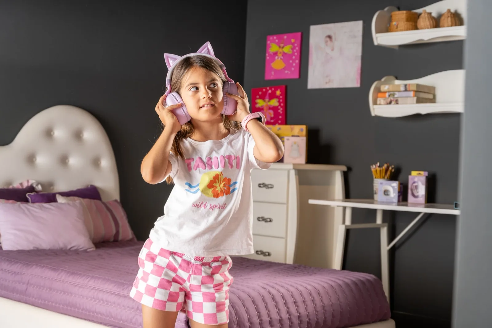 Child in printed pyjamas standing on a bed wearing cat-ear headphones