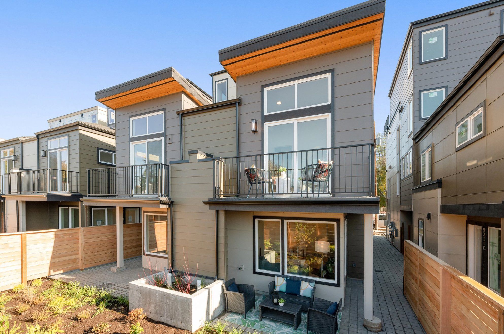Clover townhomes from the shared walkway: cedar soffits, balconies, and a ground-floor patio