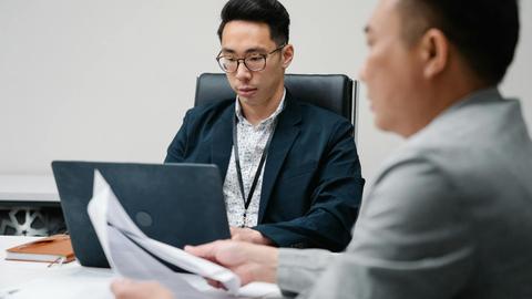 Two business professionals focused during a meeting, working on laptops and documents.