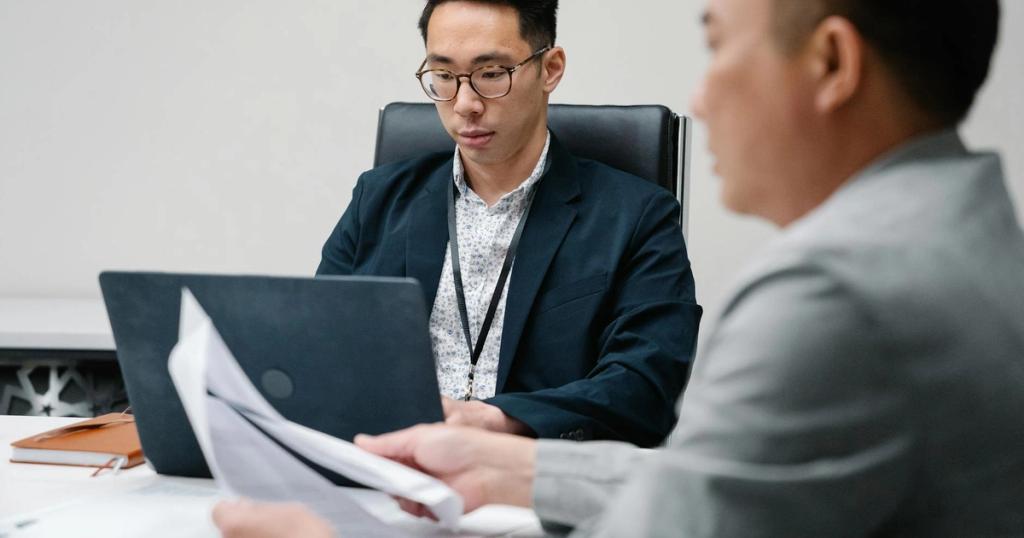 Two business professionals focused during a meeting, working on laptops and documents.